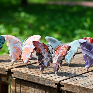 May include: A row of six butterfly-shaped ornaments crafted from various polished gemstones, including blue, peach, red, white, and purple varieties. Each butterfly features wire-wrapped bodies and wings made from natural stone slices with distinct patterns.