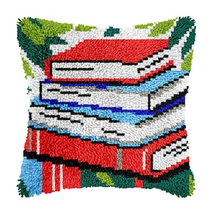 May include: Square cushion featuring a stack of books design. The books are red, white, and blue, with black and white details. The cushion has a textured, tufted appearance, with green and white accents.