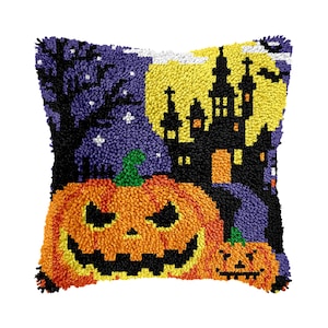 May include: A square throw pillow featuring a textured punch needle design of a Halloween scene. The image displays a large orange jack-o'-lantern in the foreground, a black haunted castle silhouette against a bright yellow moon, and a dark tree.