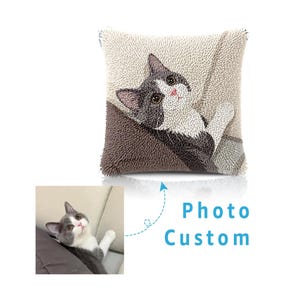 May include: A square throw pillow featuring a textured punch needle design of a grey and white cat looking upward. The cat has dark grey ears, a white face, and a grey body. Below the pillow is a reference photo of the same cat and the text Photo Custom.