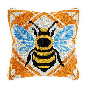 May include: Square decorative pillow with a bee design. The pillow features a large bee with black and yellow stripes, blue wings, and a black head. The background is orange and white, with a geometric pattern. The pillow is made of a textured material.