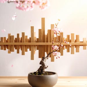 以下が含まれることがあります： ピンクの花が咲く盆栽が、濃い灰色の陶器鉢に植えられ、木製の台の上に置かれています。上部には、都市景観に似た木製の彫刻が壁に取り付けられています。ピンクの花びらが優しく落ちています。
