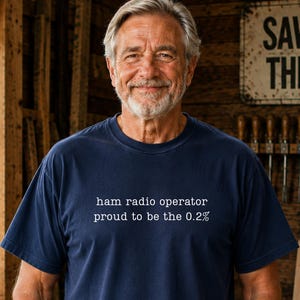 May include: A navy blue short-sleeved t-shirt featuring white text printed on the chest that reads: ham radio operator proud to be the 0.2%. The shirt has a crew neckline and a standard fit, constructed from a solid-coloured cotton fabric.