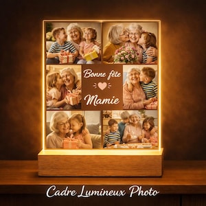 Peut inclure: Un cadre photo lumineux avec une base en bois, affichant plusieurs photos de famille. Le texte "Bonne fête Mamie" est affiché au centre. Le bas du cadre indique "Cadre Lumineux Photo".