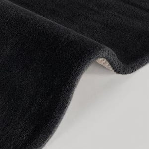 May include: A thick, charcoal gray rug with a soft, plush, high-pile texture. The rug is folded over to reveal a light-colored, woven backing material underneath the dense, dark-colored fibers that cover the entire top surface.
