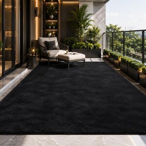 May include: A large, rectangular, solid black area rug with a plush, textured surface. The rug is positioned on a smooth, light-colored floor, covering a significant portion of the space in front of a seating area on a balcony.