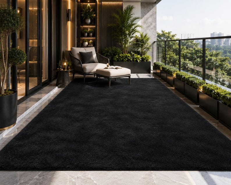 May include: A large, rectangular, solid black area rug with a plush, textured surface. The rug is positioned on a smooth, light-colored floor, covering a significant portion of the space in front of a seating area on a balcony.