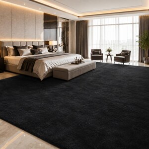 May include: A large, solid black area rug with a dense, plush texture covering the floor of a bedroom. The rectangular rug features a uniform dark color and a soft, deep pile surface that extends across the room, contrasting with the light flooring.