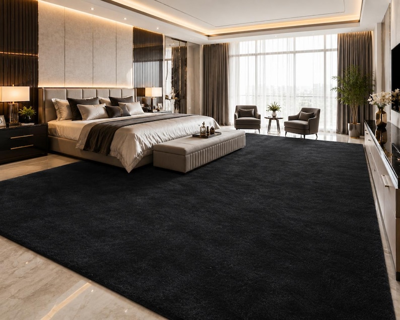 May include: A large, solid black area rug with a dense, plush texture covering the floor of a bedroom. The rectangular rug features a uniform dark color and a soft, deep pile surface that extends across the room, contrasting with the light flooring.