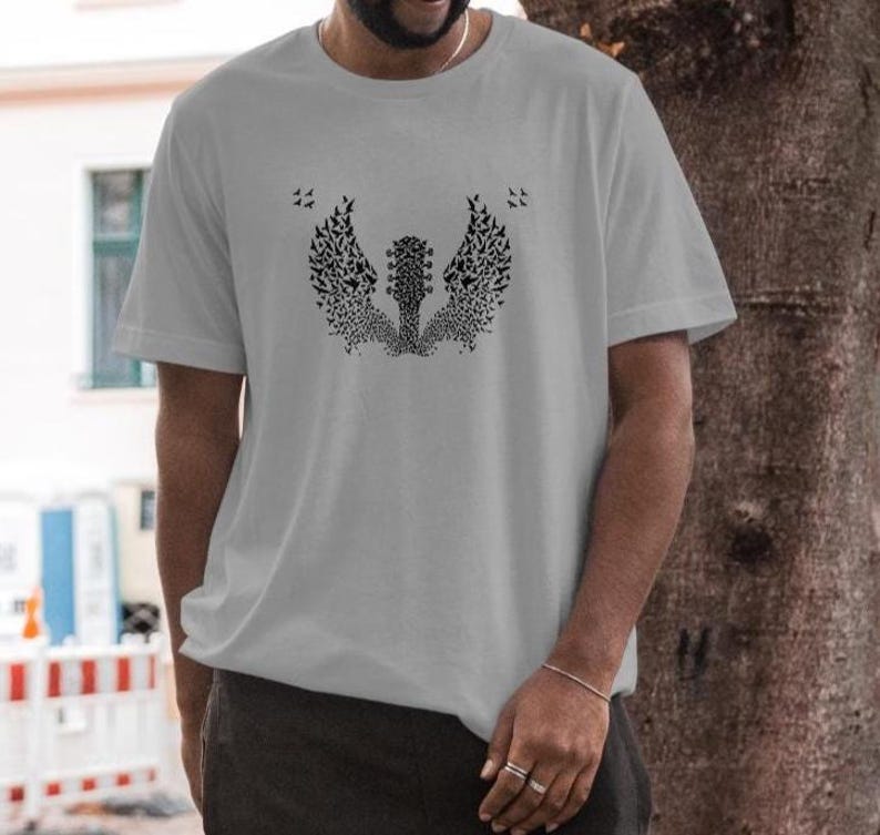 Op de afbeelding: Een lichtgrijs t-shirt met een zwarte afbeelding van een gitaar met vleugels gemaakt van kleine vogels. Het ontwerp is gecentreerd op het shirt. Het shirt heeft korte mouwen en een ronde hals.