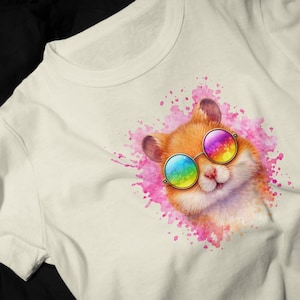 May include: Off-white t-shirt featuring a watercolor illustration of a hamster wearing rainbow-colored sunglasses. The hamster is set against a pink watercolor splash background. The t-shirt has a crew neck.