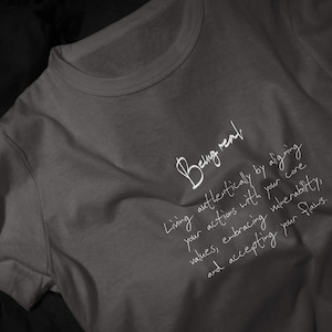 Op de afbeelding: Een grijs t-shirt met de handgeschreven tekst "Being real". Daaronder staat een langere tekst over authentiek leven, het afstemmen van je acties op je kernwaarden en het accepteren van je fouten.