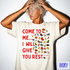 Puede incluir: Camiseta de color marfil con el texto rojo "COME TO ME... I WILL GIVE YOU REST" y una colección de ilustraciones de sillas coloridas. También se incluye el texto "Matthew 11:28".