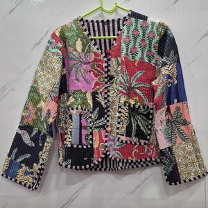 May include: A long-sleeve quilted jacket featuring a patchwork design with various floral, palm leaf, and animal prints in shades of red, green, pink, blue, and black. The jacket has a V-neckline, two front pockets, and three round buttons.