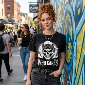 May include: A black short-sleeve t-shirt featuring a white graphic print of a skull wearing a bandana, giving the middle finger with both hands, and the text "WHO CARES" printed in a bold, stylized font below the skull illustration.