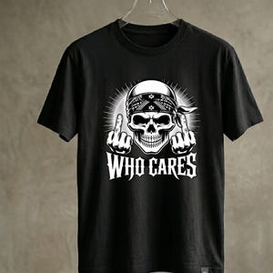 May include: A black short-sleeve t-shirt featuring a white graphic print of a skull wearing a bandana. The skull is shown with both hands raised, each displaying a middle finger. Below the skull, the text WHO CARES is printed in white.