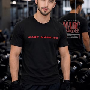 May include: A black short-sleeved crew neck t-shirt featuring the text MARC M&Aacute;RQUEZ in red lettering on the chest. The back of the shirt displays the text MOTO GP TEAM MARC M&Aacute;RQUEZ in red and white print. The shirt is worn with black fingerless gloves.