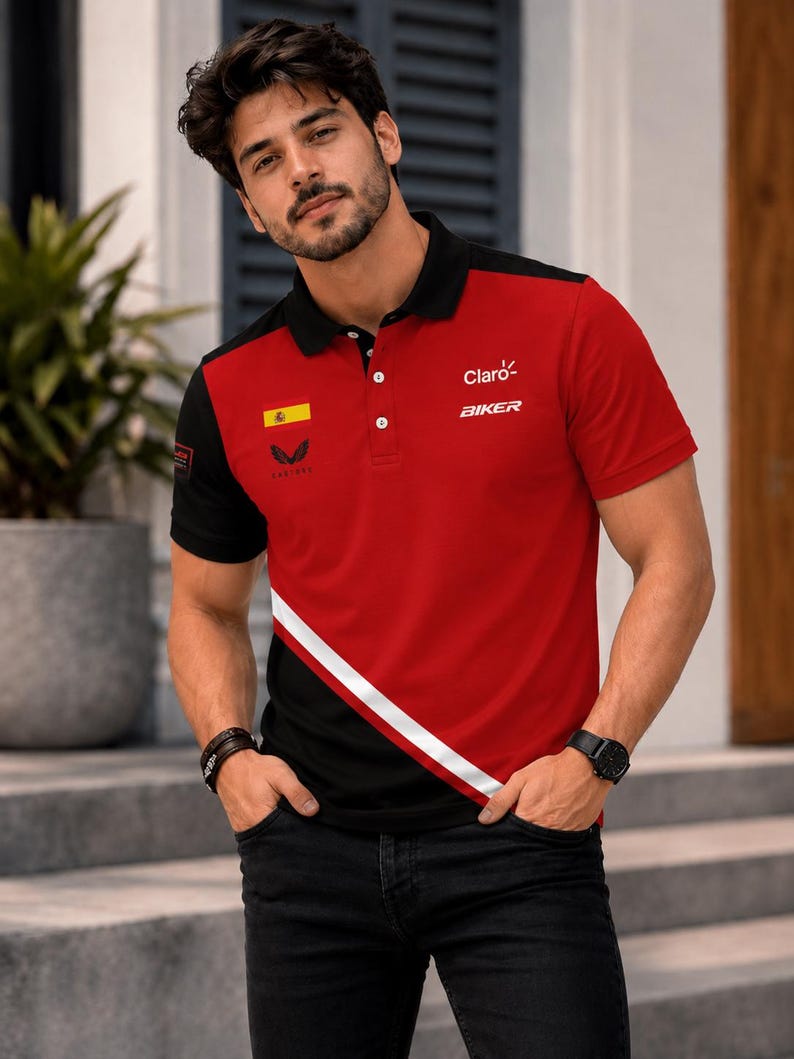Op de afbeelding: Een rood en zwart poloshirt met korte mouwen, voorzien van een witte diagonale streep, een zwarte kraag met knopen en de tekst Claro en BIKER op de borst. Het shirt toont ook een kleine Spaanse vlag en een logo aan de voorzijde.