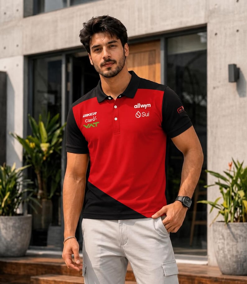 May include: A short-sleeved polo shirt featuring a color-blocked design in red and black. The shirt includes a collar with three buttons and various printed logos, including BIKER, Claro, VAT, allwyn, and Sui, displayed on the chest area.