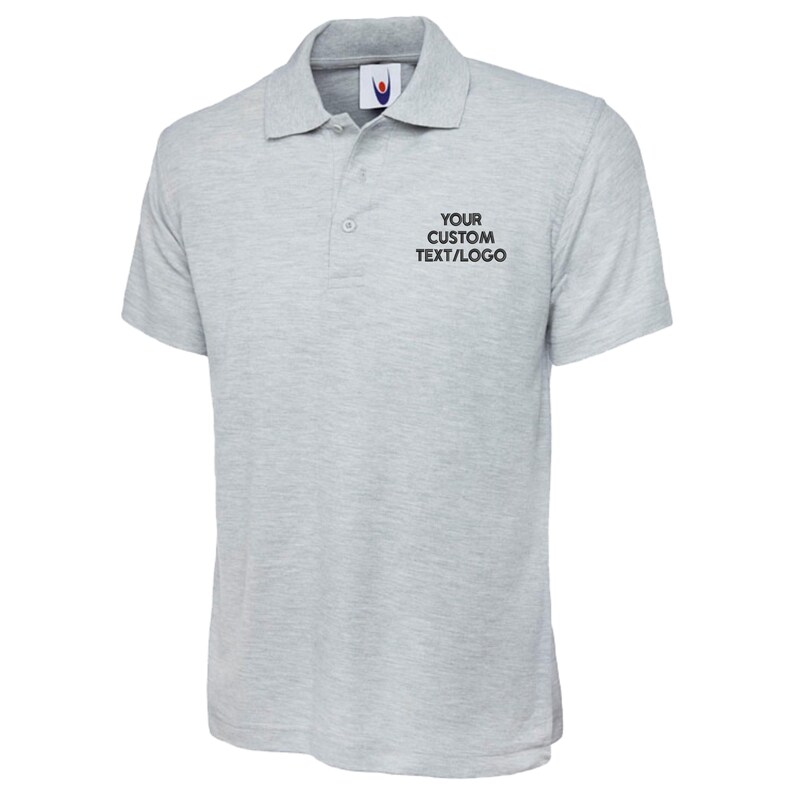 May include: Pale grey polo shirt with short sleeves and a collar. The shirt features a two-button placket and a small logo on the chest. The text "YOUR CUSTOM TEXT/LOGO" is printed on the right chest.