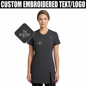 May include: Charcoal grey tunic with a diagonal zip and short sleeves. The top has the text "CUSTOM EMBROIDERED TEXT/LOGO" at the top and a logo that says "3R EQUINE THERAPY" on the left side. The tunic also has the "3R EQUINE" logo on the chest.