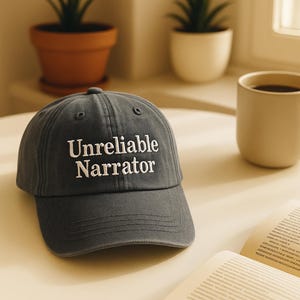 Puede incluir: Gorra de béisbol gris con la inscripción bordada "Unreliable Narrator" en blanco. La gorra tiene una visera curva y está hecha de un material suave. Un accesorio casual.