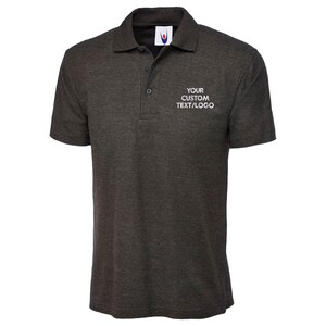 May include: Dark grey polo shirt with a collar and short sleeves. The shirt features a three-button placket and the text "YOUR CUSTOM TEXT/LOGO" on the chest. Made from a soft, textured fabric.