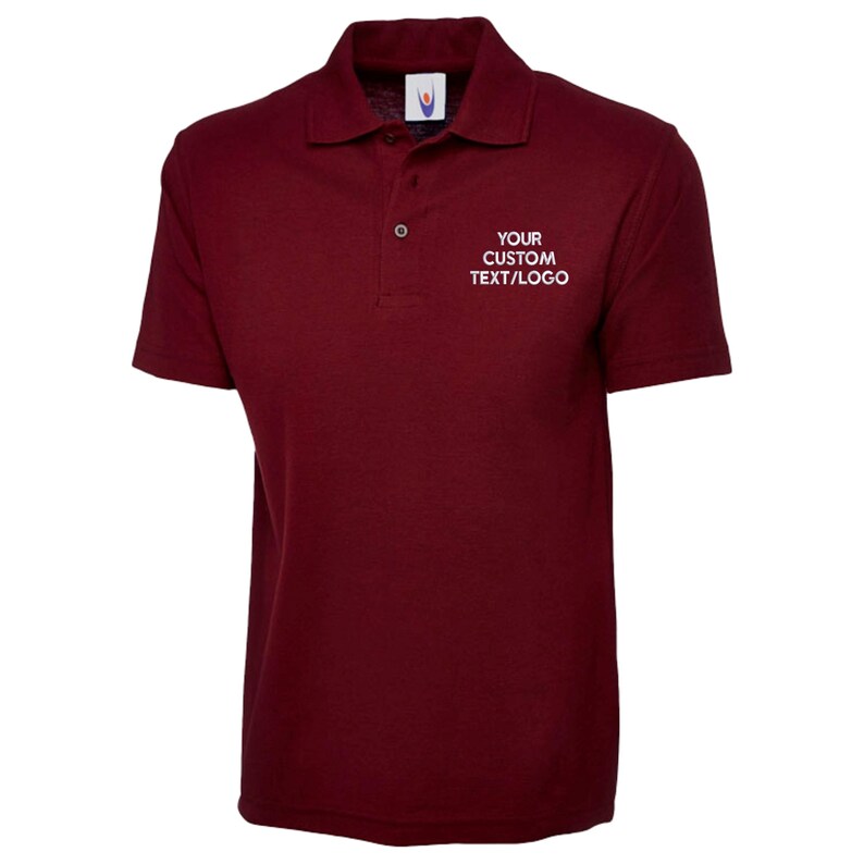 May include: A maroon polo shirt with short sleeves and a collar. The shirt features a three-button placket and the text "YOUR CUSTOM TEXT/LOGO" in white on the chest. The shirt is made of a soft, breathable fabric.