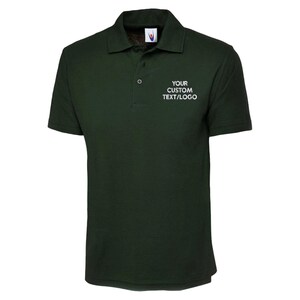 May include: Dark green polo shirt with short sleeves and a collar. The shirt features a three-button placket and the text "YOUR CUSTOM TEXT/LOGO" in white on the chest. Made from a soft, breathable fabric, suitable for various activities.