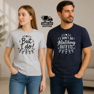 May include: A light grey t-shirt with black text reading But I do! above a string of lights, and a navy blue t-shirt with white text reading I DON'T DO MATCHING OUTFITS above a string of lights. Both shirts feature short sleeves and crew necks.