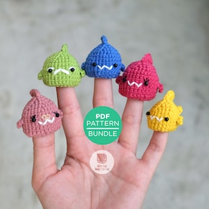 May include: A hand displays five colorful, crocheted shark finger puppets. The sharks are green, blue, pink, red, and yellow, each with embroidered details. The image includes a circular graphic that reads "PDF PATTERN BUNDLE".