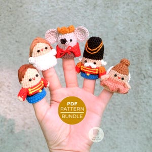 May include: A hand displaying five colorful, crocheted finger puppets. The puppets include a mouse, a soldier, and other characters, each with unique outfits and features. The puppets are in red, blue, white, and brown. The image also includes the text "PDF PATTERN BUNDLE".