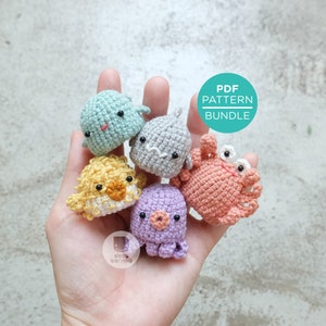 May include: A collection of six handmade crochet sea creatures in various colors, including a blue whale, gray seal, yellow pufferfish, coral crab, and purple octopus. The image includes a PDF pattern bundle graphic.
