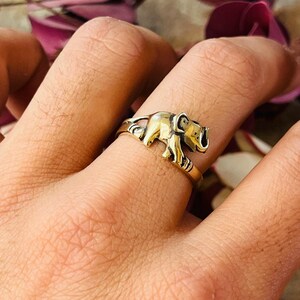 May include: A gold-coloured ring with a detailed elephant design. The elephant is shown walking, with intricate detailing on its body and trunk. The ring is worn on a finger, showcasing the jewellery's design and craftsmanship.