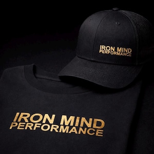 Może przedstawiać: Czarna koszulka i czapka bejsbolowa ze złotym napisem "IRON MIND PERFORMANCE". Czapka ma siatkowy tył. Koszulka ma okrągły dekolt. Przedmioty są prezentowane na czarnym tle.