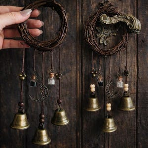 Puede incluir: Dos atrapasueños rústicos con un diseño de corona de ramitas naturales. Cada uno presenta campanas de bronce colgantes, viales de vidrio, cuentas de madera y un dije de media luna. Fondo de superficie de madera oscura.