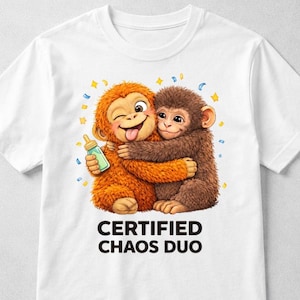 Könnte beinhalten: Weißes T-Shirt mit einer Cartoon-Illustration von zwei sich umarmenden Affen. Einer ist orange und hält eine Flasche, der andere ist braun. Der Text "CERTIFIED CHAOS DUO" ist unter dem Bild aufgedruckt.