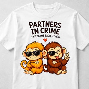 Könnte beinhalten: Weißes T-Shirt mit zwei Comic-Affen, die Sonnenbrillen tragen. Ein Affe ist orange, der andere braun. Der Text "PARTNERS IN CRIME (WE BLAME EACH OTHER)" ist über den Affen aufgedruckt.