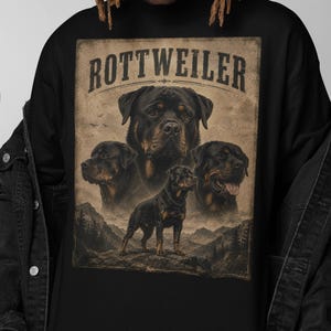 Könnte beinhalten: Schwarzes Langarmshirt mit einem Grafikdesign im Vintage-Stil von Rottweiler-Hunden. Das Design enthält das Wort "ROTTWEILER" oben, mit mehreren Hundeporträts und einem Berglandschaftshintergrund.