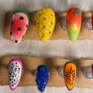 May include: A selection of fruit-themed nail art designs. The nails are decorated with watermelon, pineapple, and other fruit designs. Each nail is painted with vibrant colours and intricate details, showcasing a playful and artistic style.