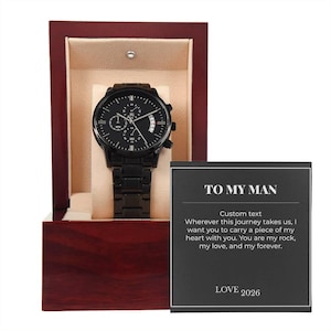 Könnte beinhalten: Eine schwarze Armbanduhr mit passendem schwarzem Metallarmband, präsentiert in einer dunklen Holzbox mit beigefarbenem Innenraum. Eine Karte mit dem Text "TO MY MAN" und einer personalisierten Nachricht ist enthalten.
