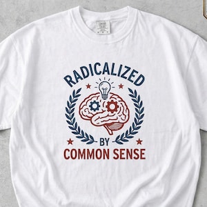 Op de afbeelding: Wit T-shirt met de tekst "RADICALIZED BY COMMON SENSE" in een cirkelvormig ontwerp met een hersen, tandwielen en een gloeilamp. Het ontwerp is in marineblauw en rood, met een lauwerkransrand. Het woord "White" staat onderaan.