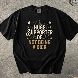 May include: Black t-shirt with gold text reading "HUGE SUPPORTER OF NOT BEING A D!CK". The design features star accents and a sunburst effect. The shirt is a crew neck and has a vintage appearance.