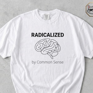 Op de afbeelding: Wit t-shirt met de tekst "RADICALIZED" boven een hersengrafiek en "by Common Sense" eronder. Het shirt heeft een ronde hals en korte mouwen. Het woord "White" staat onderaan gedrukt.
