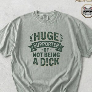Puede incluir: Camiseta gris claro con el texto "HUGE SUPPORTER OF NOT BEING A D!CK" en verde oscuro. El texto está dispuesto en un diseño llamativo. La camiseta tiene mangas cortas y cuello redondo.