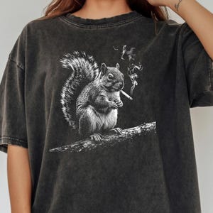 Peut inclure: T-shirt gris foncé surdimensionné avec une illustration en noir et blanc d'un écureuil fumant une cigarette. L'écureuil est perché sur une branche. Le mot "Pepper" est imprimé en gras noir en bas.