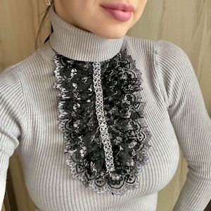 May include: A gray turtleneck sweater with a black lace trim around the neckline. The lace trim has a silver sparkle.