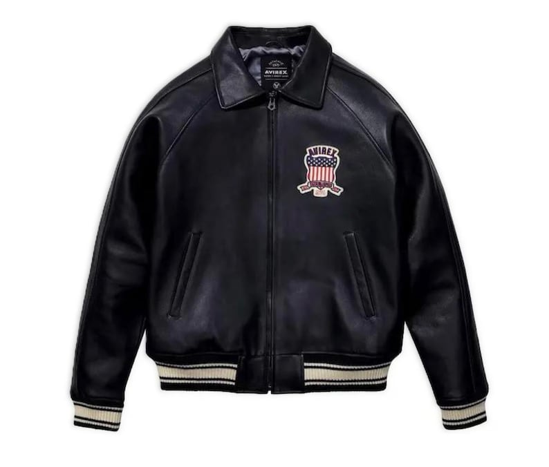 May include: Black leather jacket with a collared neckline, zipper closure, and a patch on the chest. The jacket features a ribbed hem and cuffs with white stripes. The patch displays a shield design with the word "AVIREX".