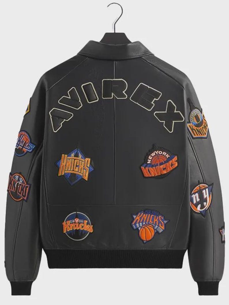 May include: A black leather jacket featuring the word AVIREX in large letters across the upper back. The jacket is decorated with multiple embroidered patches of the New York Knicks basketball team logo in orange, blue, and white colors.