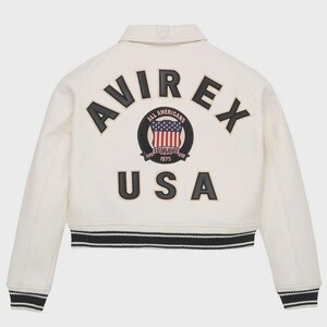 May include: Cream-colored jacket with black and white striped trim. The back features the word "AVIREX" in black letters above a circular emblem with a US flag design and the word "USA" in black letters.